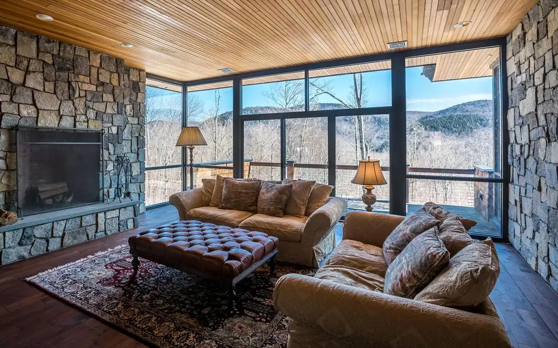 Living room with stone walls, a wood ceiling and floor-to-ceiling glass facing the mountains