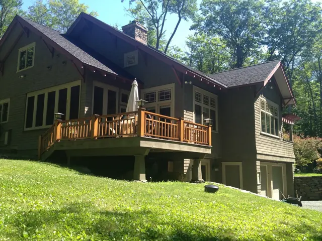 Dark shingle home with a wraparound deck over a green lawn
