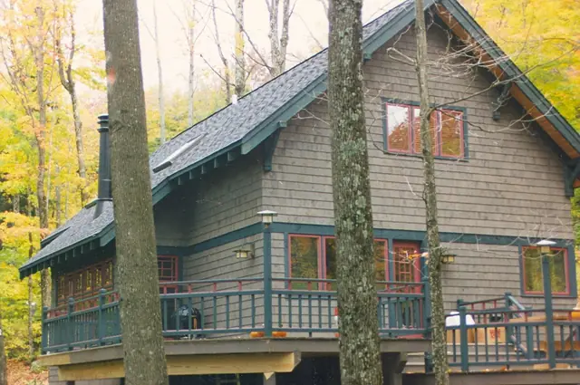 Green craftsman home with a wraparound porch among tall trees