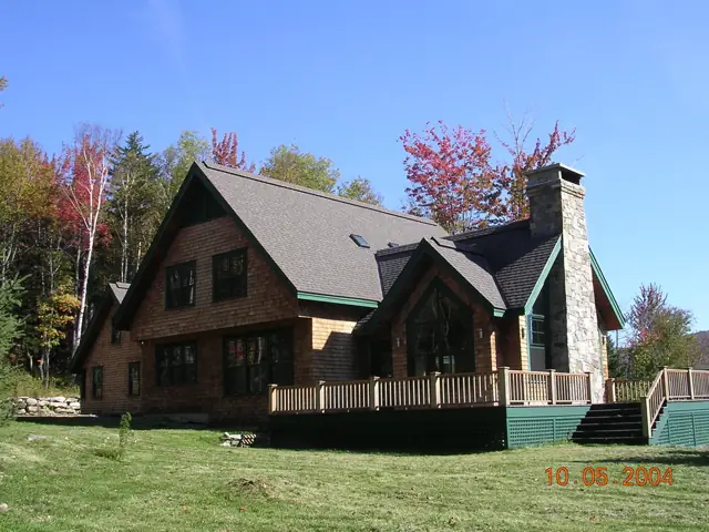Shingle home with stone chimney and autumn foliage