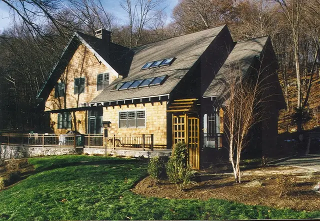 Shingle-style home with stone base and dormers set in a wooded Vermont lot