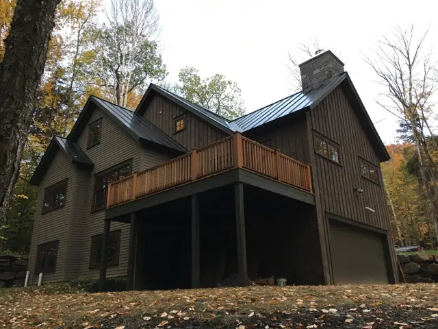 Gray home with a raised deck among autumn trees