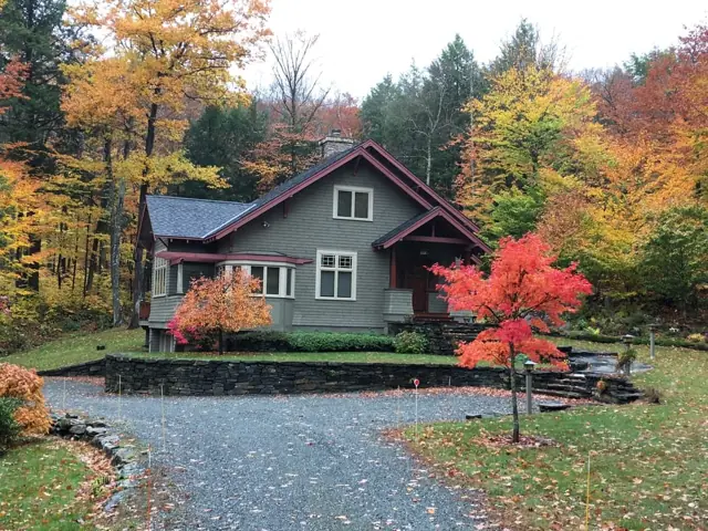 Green home on a curving drive surrounded by fall color